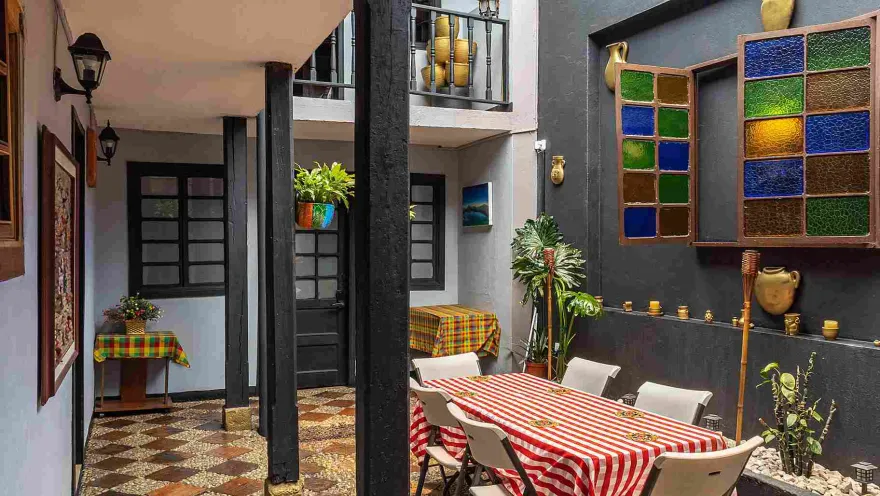 Patio interior de Villacandelaria Hostel, con mesas decoradas, plantas, detalles artesanales y espacios comunes de estilo colonial.