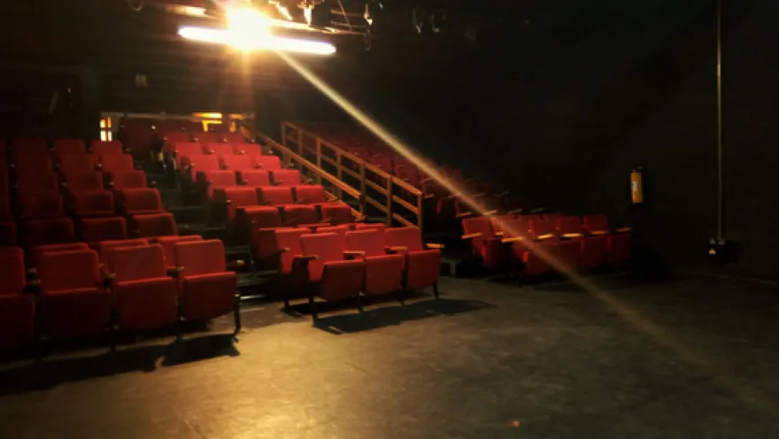 Theater hall with rows of red chairs, scenic lighting, and a space set up to enjoy a performance.