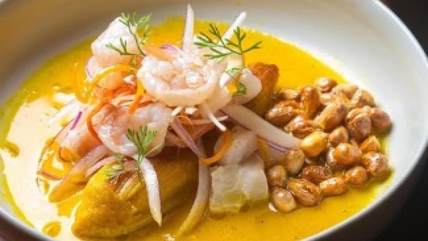Plato de cocina peruana con pescado y camarones, acompañado de cebolla, ají, hierbas frescas y maíz tostado.