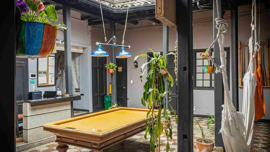 Zona común del hostal con mesa de billar, hamacas, plantas ornamentales y recepción, ideal para descansar y socializar.