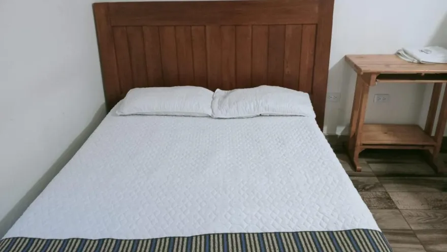 Habitación privada con cama doble, cabecero de madera, ropa de cama blanca y mesa auxiliar.