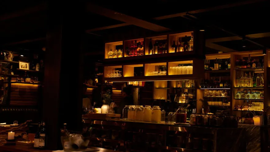 Interior del restaurante El Chato, con mobiliario de madera, estanterías de bebidas e iluminación cálida que crea un ambiente íntimo y acogedor.