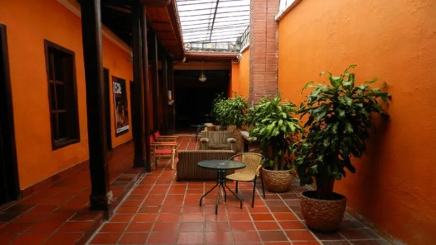 Interior courtyard with colonial architecture, orange walls, wooden corridors, ornamental plants, and tables creating a cozy and peaceful atmosphere.