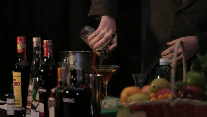  Persona preparando un cóctel con bebidas, frutas y utensilios de bar.