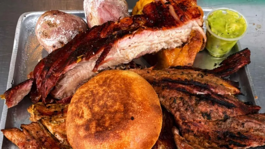 Plato de aluminio con cortes de carne a la parrilla, costilla crocante, arepa de maíz dorada y salsa de ají verde.