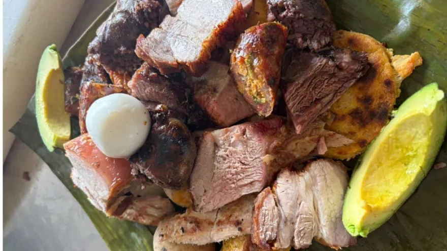 Plato fuerte de picada asada servida sobre hoja de plátano con embutidos, huevo de codorniz y aguacate fresco.   