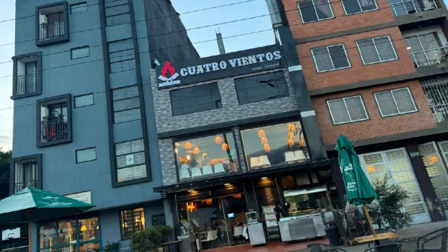 Fachada de dos pisos con ventanales de vidrio, iluminación cálida y letrero de Cuatro Vientos en la parte superior.