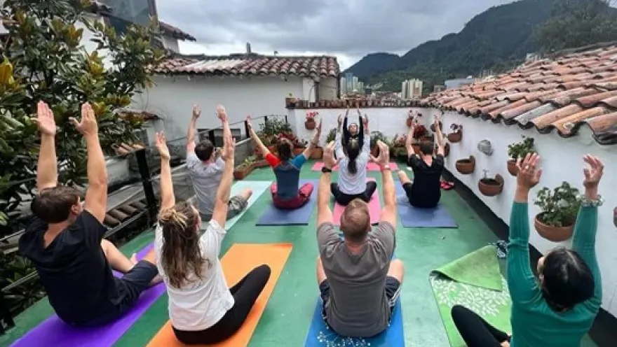 Grupo de personas practicando yoga en una terraza al aire libre, con colchonetas de colores y vistas a las montañas.