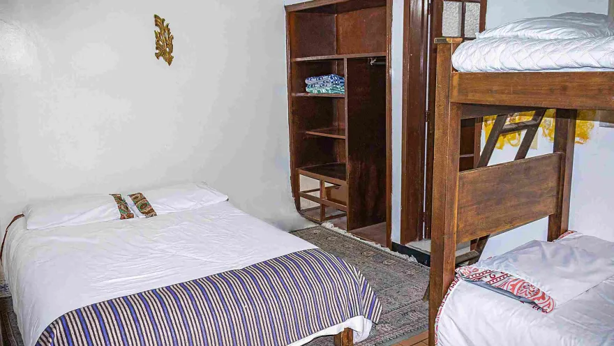Habitación compartida con camas individuales y dobles, mobiliario de madera y decoración sencilla y acogedora.