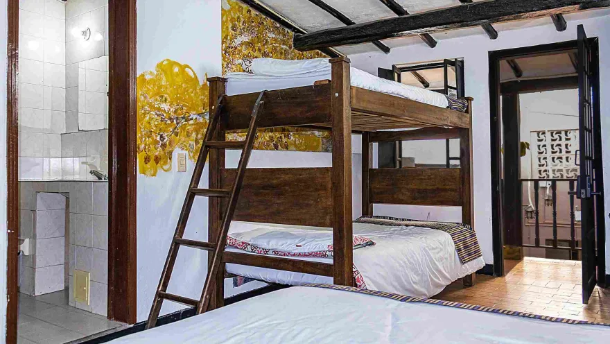 Habitación compartida con literas de madera, camas tendidas y baño privado, ideal para alojar a varios viajeros.