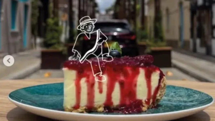 Tajada de pastel de queso bañada en salsa roja en un plato turquesa con un dibujo animado blanco superpuesto de personaje.   