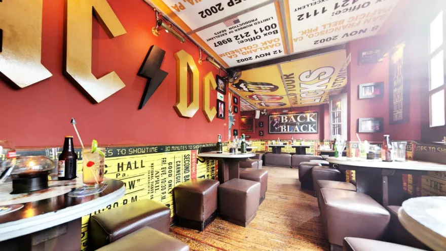 Salón ambientado con decoración de bandas de rock, letras luminosas en pared roja y mesas servidas con cócteles.