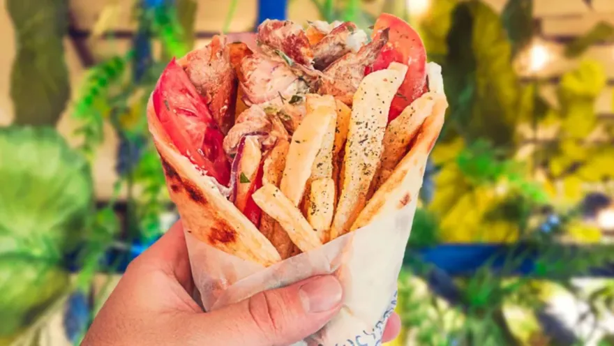 Primer plano de un sandwich griego en pan pita suave repleto de pollo, papas a la francesa y vegetales frescos.   