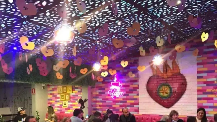 Comedor concurrido adornado con corazones colgantes, lámparas redondas y mural colorido de corazón de fuego.   