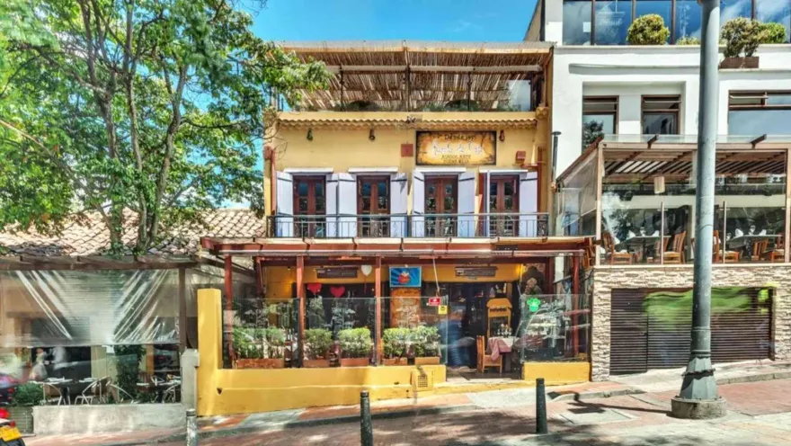 Edificación de color amarillo con ventanas de madera, terraza en el tejado y letrero de La Tienda de Café sobre la calle.   