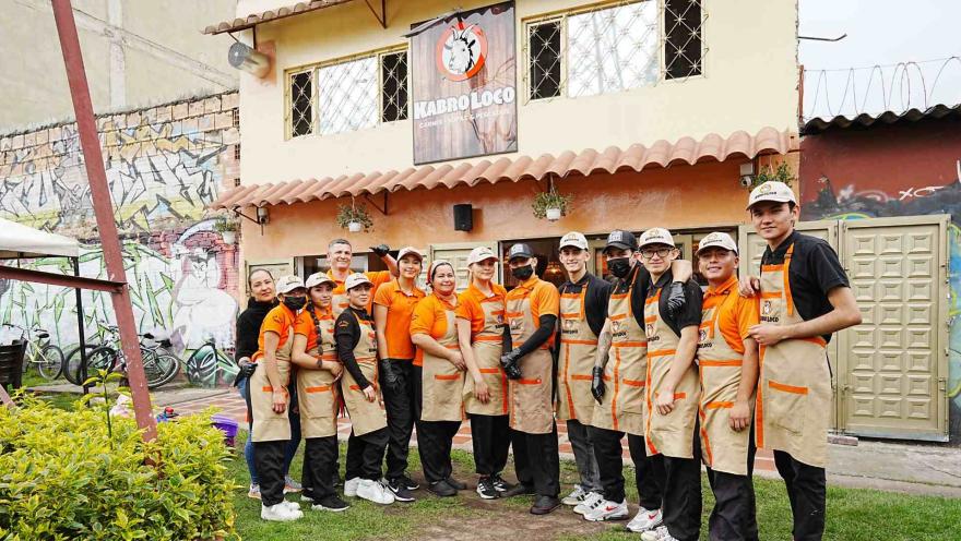 Grupo de colaboradores con uniformes naranjas y delantales posan sonrientes frente al restaurante Kabro Loco.   
