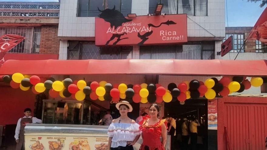 Dos mujeres vestidas con trajes típicos posan bajo una guirnalda de globos en la entrada de Asaderos Alcaraván.