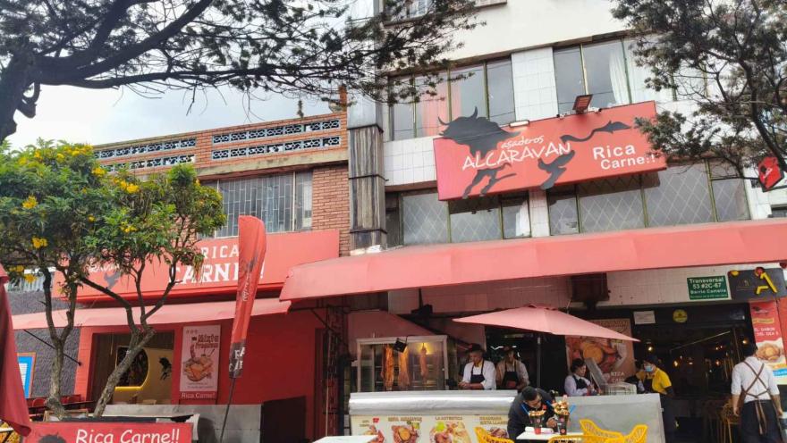 Fachada del restaurante Asaderos Alcaraván de color rojo con su letrero comercial y personas en la entrada.