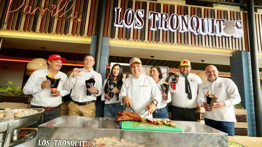 Grupo de personas posa con conos de picada tras el chef que corta lechón asado frente al restaurante Los Tronquitos