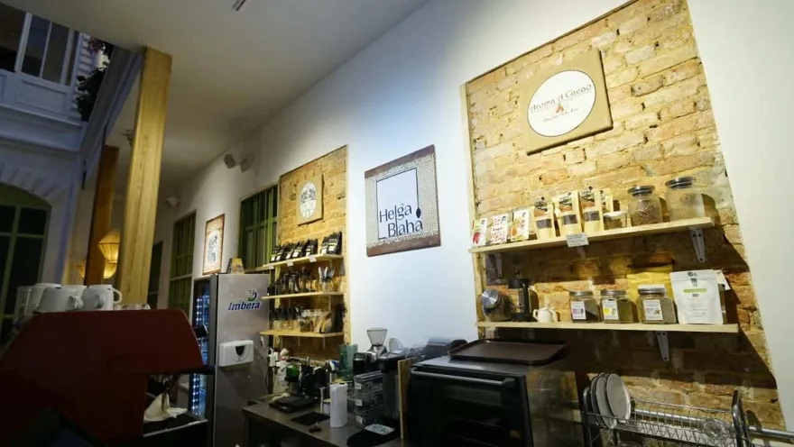 Estantes de madera sobre pared de ladrillo con empaques de café, frascos de cristal y aviso de Helga Blaha en la pared.  