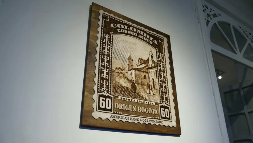 Cuadro de madera con diseño de estampilla postal antigua que dice Colombia Correo Aéreo Origen Bogotá sobre pared clara. 