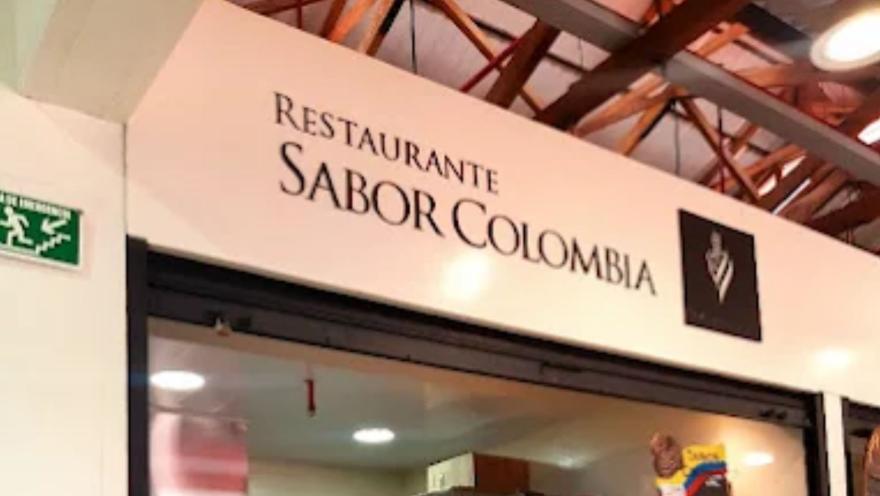  Aviso letrero blanco en la entrada de un local con el texto "Restaurante Sabor Colombia" en letras oscuras.