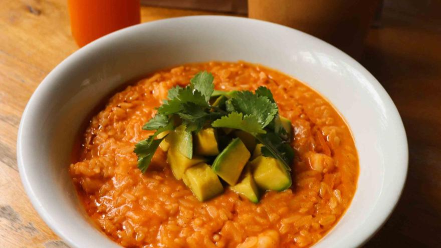 Plato de arroz cremoso con camarones, aguacate y cilantro fresco, servido en un tazón blanco sobre una mesa de madera.