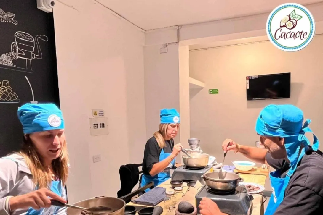 Dos mujeres y un hombre con delantales y gorros azules calientan cacao en sendas ollas.