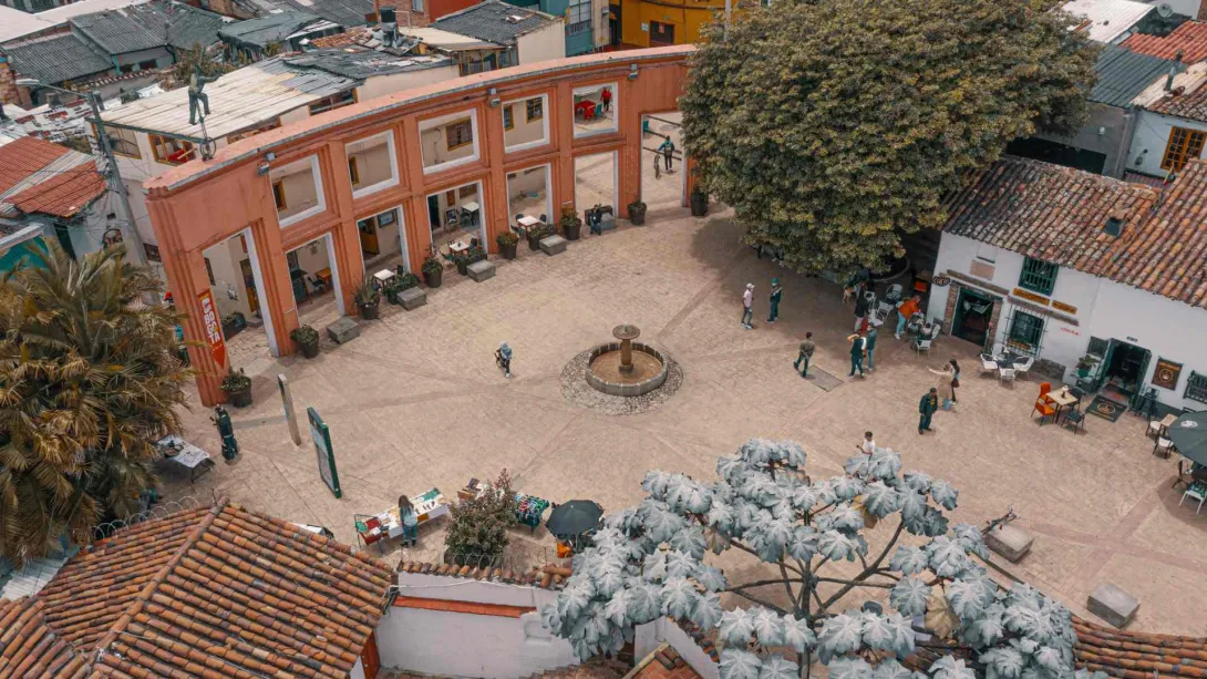 Chorro de Quevedo Square, wide aerial shot taken by drone showing the tiled rooftops of surrounding buildings, three trees around the square, and several people gathered.
