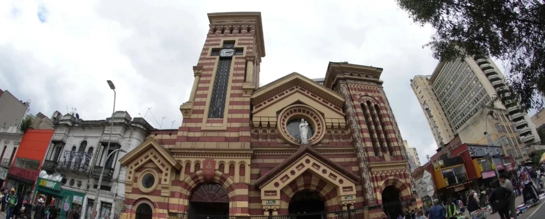 Church of Our Lady of the Snows, panoramic view of the façade with old buildings on both sides and a few people walking nearby. 