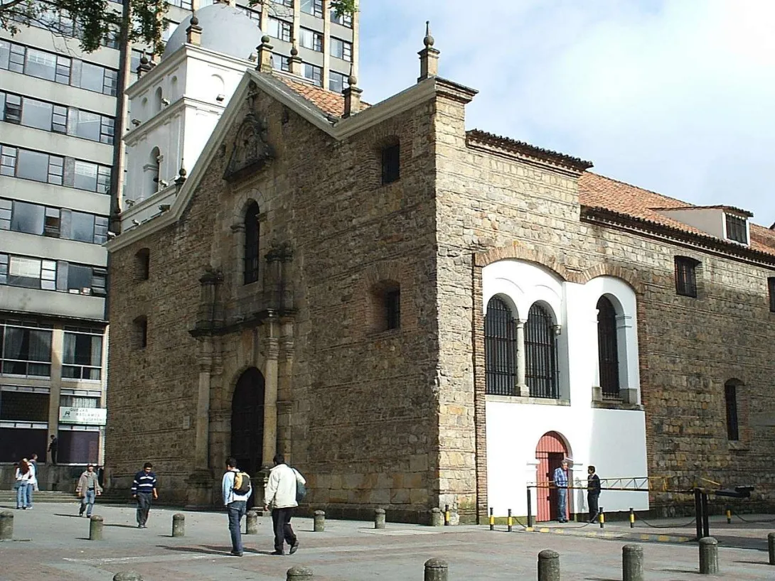  Church of St. Augustine, a view of the facade and left side, featuring the grand central door, a side entrance, and large windows. A modern building stands in the background as people walk by the front.