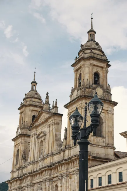 Catedral Primada vista lateral de la parte alta y sus torres con campanas. Con cielo azul grisaceo sobresale un farol negro antiguo con dos farolas de luces.