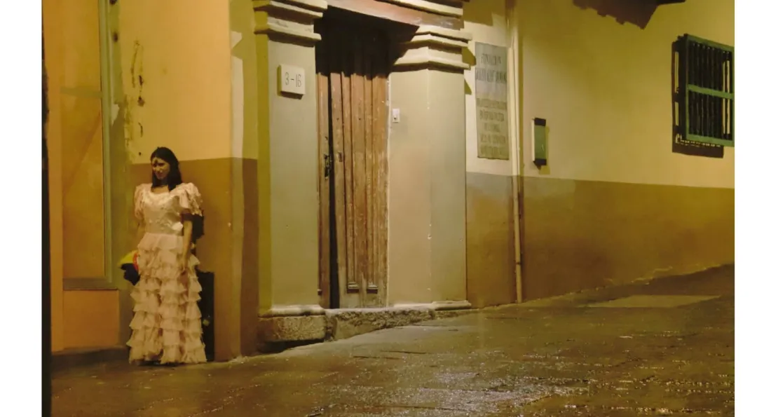  Mujer con cara de demonio y vestida con ropa antigua, detrás de una pared en una calle desolada.