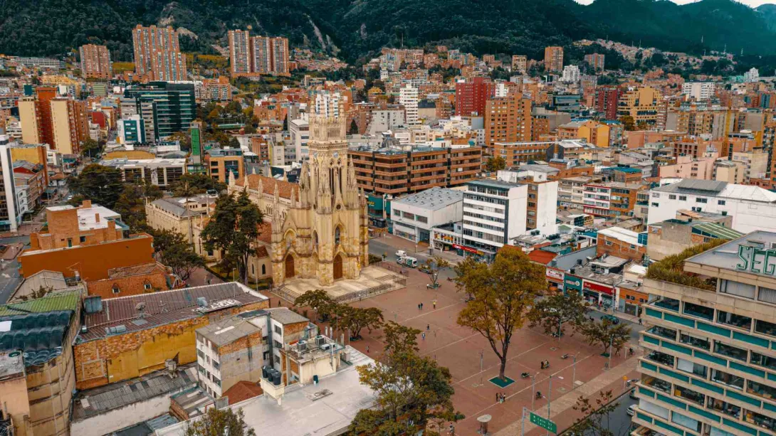.Iglesia Lourdes gótica plano general de la calle 63 con carrera 13 con los techos de las muchas edificaciones incluso en los cerros orientales. Se ve desde arriba la plazoleta de Lourdes, algunas personas pequeñas, unlos cuantos árboles, dos muy altos y los edificios circundantes.