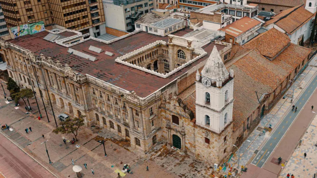  Iglesia San Francisco colonial con el techo, desde arriba con drone, al lado de edificación republicana en la carrera séptima con Avenida Jimenez y algunas pequeñas personas caminando alrededor.  
