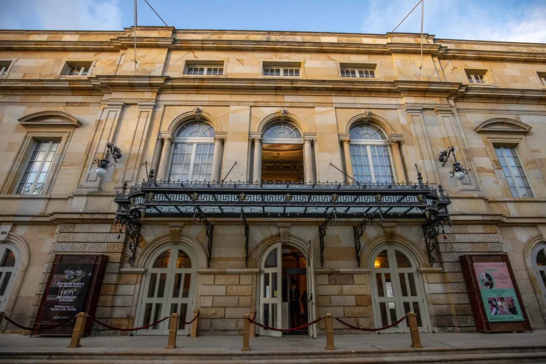 Teatro Colón, general view of the façade with the first and second-floor doors open. Neoclassical architecture with ornamental and functional details in carved stone, featuring its horseshoe shape. On both the left and right sides, there is a promotional sign.