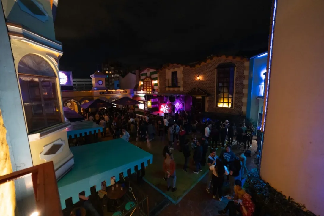Theatron - internal square at night, featuring iconic castle-like facades, and people talking.