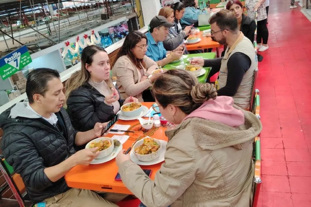 Grupo de personas en un restaurante de una plaza de mercado comiendo productos tradicionales colombianos como sancocho y frijolada.
