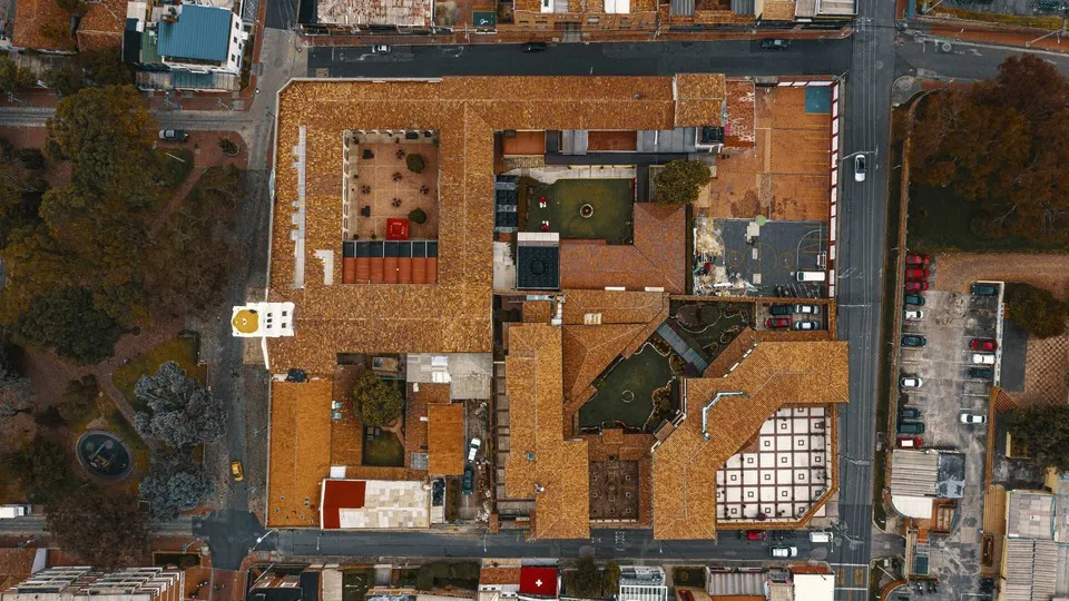 Vista aérea de un conjunto arquitectónico colonial en Usaquén, Bogotá. Los techos de teja roja resaltan entre calles estrechas y árboles que rodean el lugar, mostrando la armonía entre la tradición y la vida urbana actual.