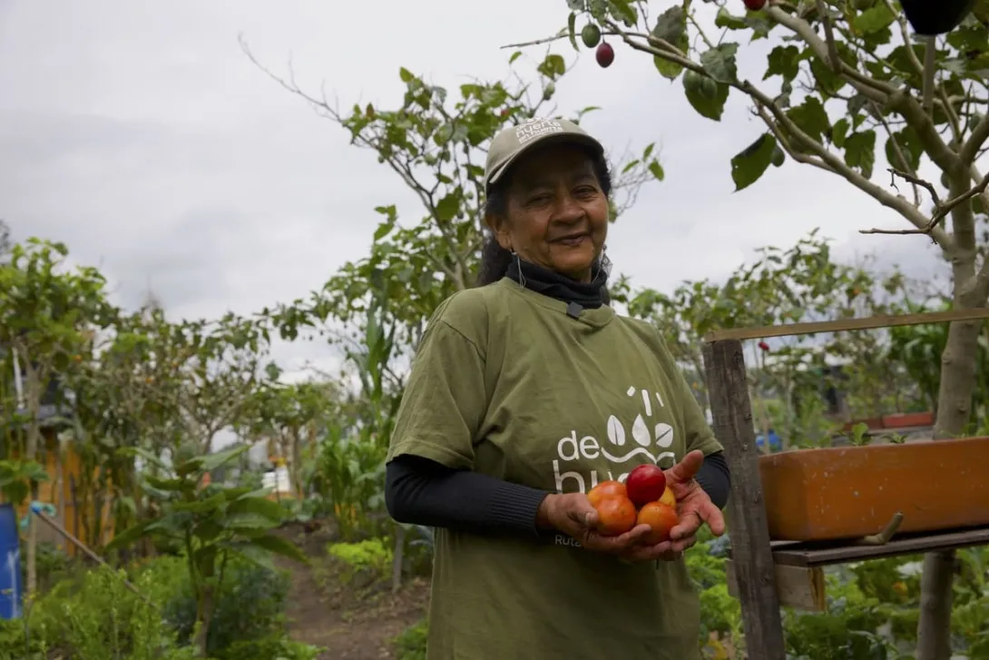  Mujer campesina sonríe y muestra productos cosechados.