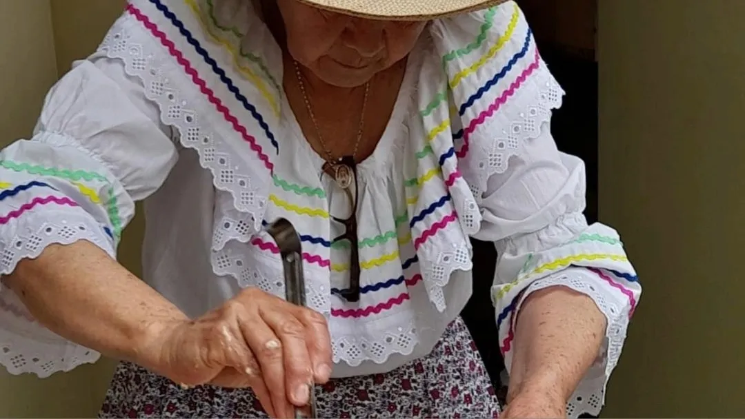 Mujer con traje típico campesino y sombrero de paja que le tapa la cara parece que está cocinando.