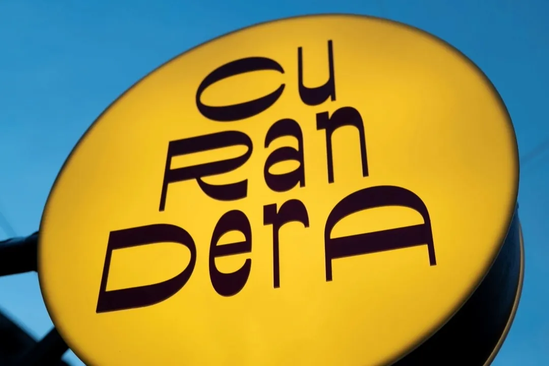  Aviso gigante de forma circular de color amarillo con letras en café que dice "curandera". 