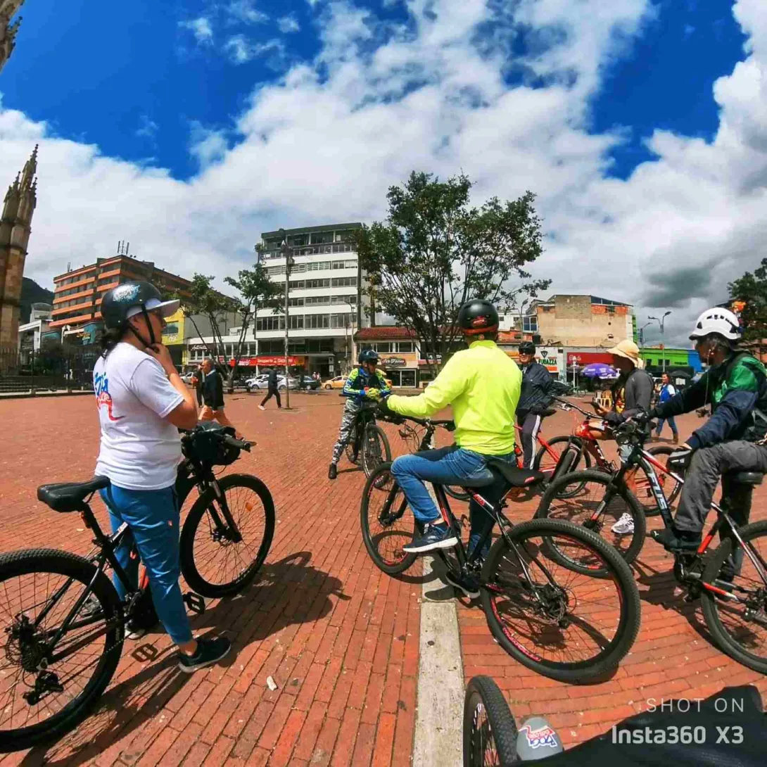 Grupo de ciclistas en la plazoleta de Lourdes, encima de sus bicicletas escucha a un guía.