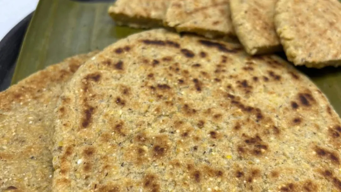 Primer plano de dos arepas doradas de trigo sobre una hoja de plátano, al fondo se ven trozos de la misma arepa.
