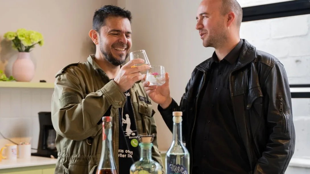 Dos hombres en un salón beben y comparten amenamente delante de tres botellas de trago.