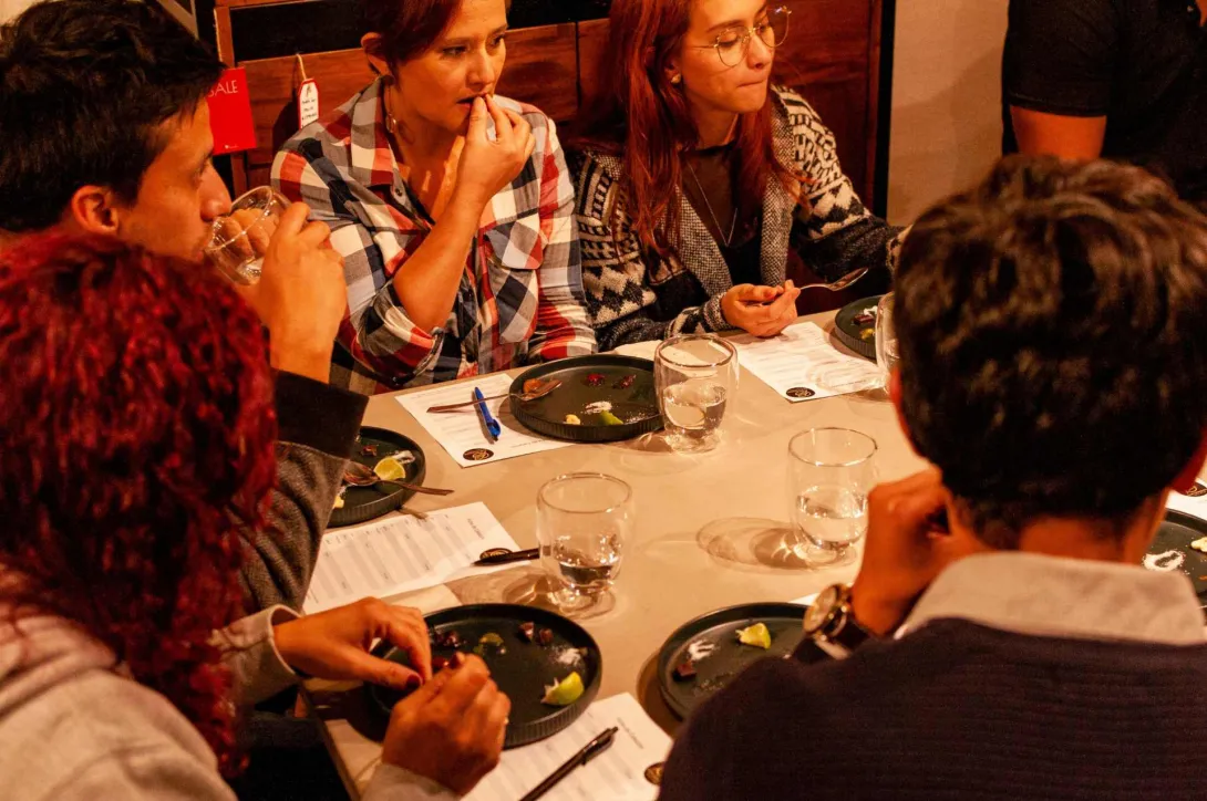 Grupo de personas jóvenes alrededor de una mesa, catando trozos de café y tomando anotaciones en una hoja de papel.