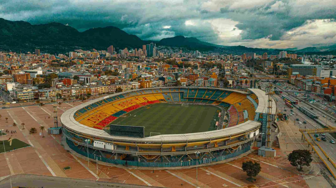 Estadio El Campín plano general visto de norte a sur con la ciudad de fondo. El cielo es gris.