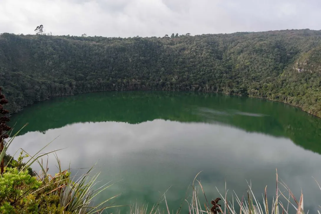 Laguna de Guatavita circular con agua verde y rodeada por frondosa vegetación.