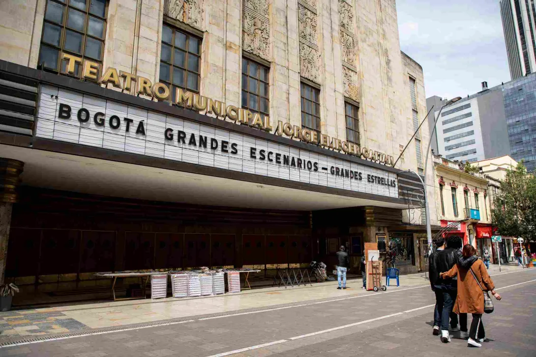 Fachada del teatro Jorge Eliecer Gaitán de día, su puerta y paredes en art decó; el aviso con el nombre en letras en mayúscula y doradas; y el aviso que anuncia las obras en fondo blanco y con letras mayúsculas en color negro. Algunas personas caminan al frente.