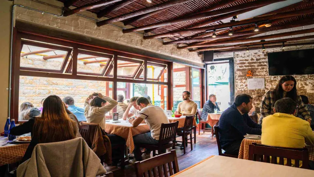 Comedor rústico con paredes de ladrillo y madera, lleno de clientes disfrutando de sus comidas en un ambiente acogedor.